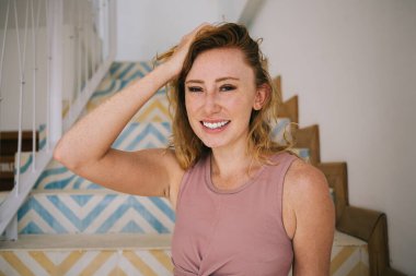 Gün ışığında renkli merdivenlerde çitlerle rahatlarken gülümseyen ve kameraya bakan genç bir kadının saçlarına dokunması.