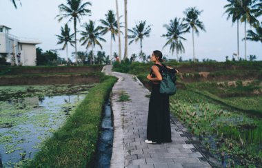 Siyah kıyafetli, kendinden emin bir kadın turist sırt çantasıyla kaldırımda duruyor ve harika manzaranın tadını çıkarırken başka tarafa bakıyor.
