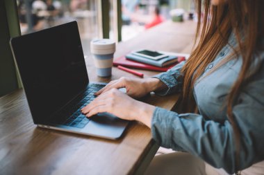 Bilgisayarda yazı yazarken ekrana bakan ve gündüz vakti kahve kalemli günlük akıllı telefonuyla masaya oturan isimsiz kadın serbest çalışanın yan görüntüsü.