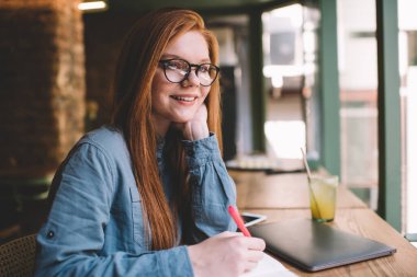 Gözlüklü, gülümseyen bir kadın kameraya bakarken el ele otururken masaya meyve suyu dolu bir bilgisayarla dokunuyor ve gündüzleri bulanık kafede kalemle yazı yazıyor.