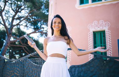 Neşe dolu etnik bayanlardan basit beyaz kıyafetler giyen, cep telefonlu yaz tatilinde dinlenirken manzaranın keyfini çıkaran.