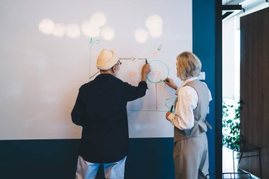 Resmi olarak tanınmayan meslektaşlarının arka planda elinde işaretler tutarken ve ofiste iş planlarını hazırlarken beyaz tahtaya şemalar çizerken