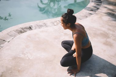 High angle full body of sportive young barefoot female in sport wear practicing Elevated Lotus pose while balancing on arms during yoga training near swimming pool clipart