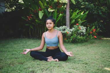 Nilüfer çiçekli poz verip meditasyon yaparken yüzünü çeviren, spor kıyafetli, rahat, genç bir kadın vücudu.