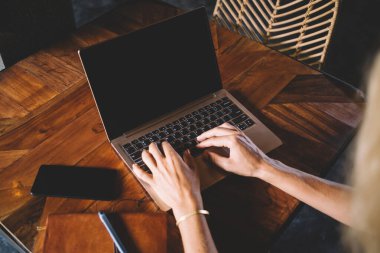 Akıllı telefon ve defterle ahşap masada otururken dizüstü bilgisayarla yazı yazan serbest çalışan kadın ekinlerden.