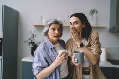 Kadınlar mutfakta elinde bir bardak sıcak içecekle dikilip kameraya bakarken dedikodular annesini afallatırken, kız da ağızlarını eliyle kapatıyor.