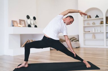 Tam boy esnek erkek sporcu. Evde sabah antrenmanı yaparken yoga yaparken vücudunu esnetiyor.