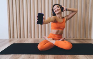Nilüfer çiçeğinde poz veren, yoga yapan ve egzersiz sırasında cep telefonuyla müzik dinleyen mutlu, ince bir kadın vücudu.