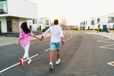 Anonim bir adam ve kadının yol boyunca koşarken günbatımının keyfini çıkarırken modern şehir caddesinde konut binalarının yanında