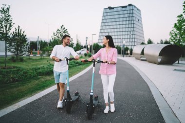 Asfalt yolda elektrikli scooterlarla yürüyen ve parkta birbirlerine bakan çok ırklı çiftlerden oluşan bir vücut.