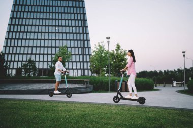 Düşük açılı, çok kültürlü, romantik bir kadın ve erkek birbirlerine bakarken şehrin caddesinde ayakta durup scooterlara biniyorlar.
