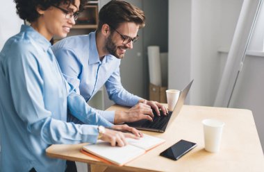 İş adamı dizüstü bilgisayarda yazı yazarken bayan meslektaşı da deftere bir şeyler okuyor ya da bakıyor. İş birliği ve takım çalışması. Beyaz ırkın milenyum insanları masamızda. Modern başarılı insanlar