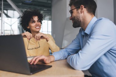 İş kadını ve işadamı laptopla çalışırken birbirlerine bakıyorlar. İş birliği ve takım çalışması. Genç Kafkasyalı milenyum insanları ofiste masa başında. Modern başarılı insanlar