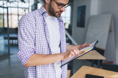 Bin yıllık Kafkas iş adamının kağıt yapıştırıcısını panoya yapıştırırken çekilmiş görüntüsü. Modern başarılı adam kavramı. Ofisteki masada gözlüklü, kablosuz kulaklıklı, odaklanmış bir adamın belirsiz yüzü.