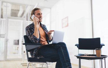 Kafası karışmış erkek programcı, modern dizüstü bilgisayarda uzaktan çalışan web başlangıç projesiyle ilgili problemleri tartışmak için meslektaşına sesleniyor. Ciddi bir adam mobil uygulamayı konuşmak ve telefon etmek için kullanıyor.