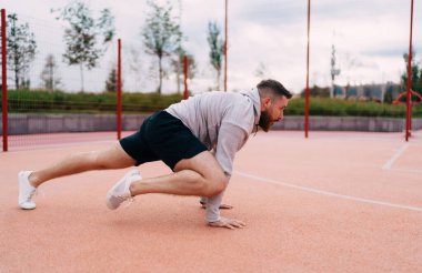 Yan görüş güçlü kaslı erkek kapüşonlu atlet antrenman yaparken metal çitlerin yanındaki stadyumun sahasında.