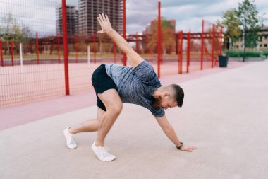 Bulutlu bir günde stadyumda spor yaparken vücudunu esneten siyah şortlu erkek sporcunun vücut manzarası.