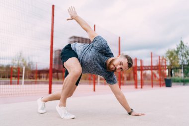 Spor kıyafetleri ve spor salonunda spor yaparken vücut esneme hareketleri yapan genç, sakallı sporcu bir erkek.