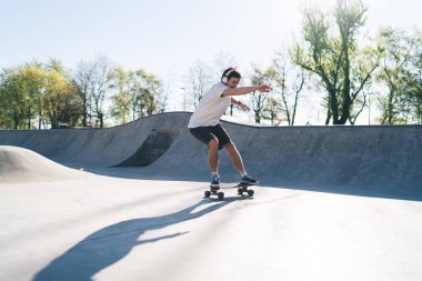 Güneşli bir günde kaykay yapan ve kulaklıkla şarkı dinleyen kaykaycı erkek kaykaycı ve kollarını rampaya dayamış.