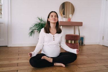 Üç aylık dönemde çıplak ayakla Padmasana egzersizi yapan ve yerde oturup meditasyon yaparken nefes alan sakin bir kadın vücudu.