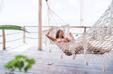 Yaz tatilinde tahta terasta hasır hamakta yatan uzun saçlı, çıplak ayaklı, genç ve zarif bir kadın vücudu.