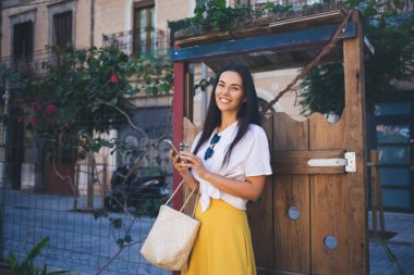 Yaz tatili boyunca kameraya gülümseyen modern hücresel cihazlı mutlu hipster kız portresi, mobil teknolojisi olan neşeli Kafkas blogcu bedava dijital zamanın tadını çıkarıyor.
