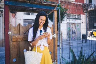 Akıllı telefon teknolojisinde, e-posta mesajlarını kontrol etmek için 4G kablosuz ağ kullanan gülümseyen beyaz kadın, neşeli kadın seyahat blogcusu, turistik metin bilgileriyle web yayını yaratıyor