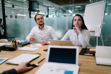 Odaklanmış iş adamları resmi giysiler içinde ahşap masada dizüstü bilgisayarlarla oturuyor ve ofis projesinde birlikte çalışırken dikkatlerini başka yöne çeviriyorlar.