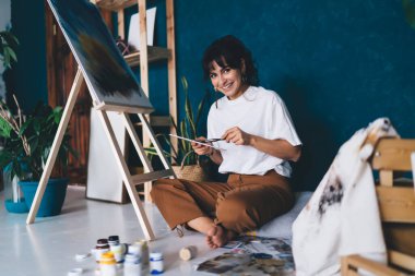 Çekici genç bayan ressam resim çiziyor ve hobisinin rahatlatıcı sürecinden zevk alıyor. Yaratıcı ve yetenekli esmer kadın sehpada resim yaratıyor. Petrolle çizim yapmayı öğrenmek