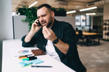 Mutsuz sakallı iş adamı, boş zamanlarında boş zamanlarında boş zamanlarında iş arkadaşlarıyla telefon görüşmelerini kaçırırken elinde not defteri ve kalemlerle masada oturuyor.