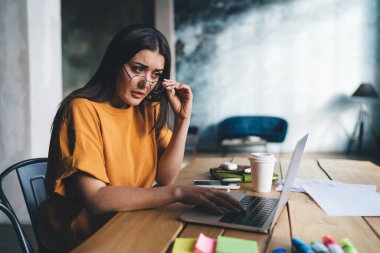 Düşünceli serbest çalışan kadın gözlüklere dokunuyor ve netbook 'a bakıyor. evde uzaktan çalışma sırasında ekrana ilgiyle bakıyor.