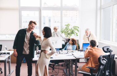 Bir grup etnik çeşitlilikte iş arkadaşı masanın etrafında toplanıp projenin detaylarını tartışırken gülümseyen iş arkadaşları masanın yanında durup yumruklarını tokuşturuyorlar.