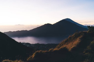 Mavi denizin yanındaki çimlerle kaplı dağ sırasının muhteşem manzarası. Sonsuz gökyüzüne karşı sabah vakti bulutlarla kaplı.