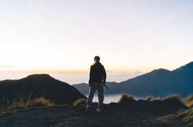 Anonim bir kadının çimenli tepede durup tatil boyunca dağlık arazide yürüyüş yaparken doğaya hayran olması.