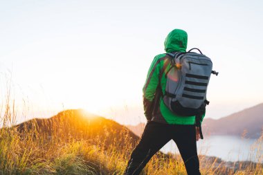 Bali 'de güneş doğarken volkanik arazide göl ve dağların manzarasına hayran olan, sırt çantalı, sıcak elbiseli, tanınmayan erkek yürüyüşçünün arka görüntüsü.