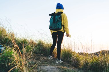 Sırt çantalı, elinde akıllı telefonuyla tepenin yamacında duran ve Batur Dağı yakınlarında yürüyüş yaparken doğanın tadını çıkaran anonim kadın yürüyüşçünün arka görüntüsü.