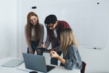 Çok ırklı ofis çalışanlarından oluşan bir ekip, çalışma ortamında iş planı üzerinde işbirliği yaparken netbook ve belgelerle gelişigüzel giyiniyor.