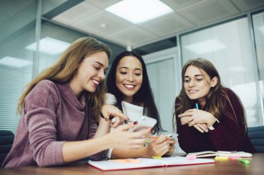 Modern ofiste başarılı bir proje üzerinde çalışırken gündelik kıyafet giymiş, beyin fırtınası yapan ve cep telefonu kullanan mutlu kadın çalışanlardan oluşan bir ekip.