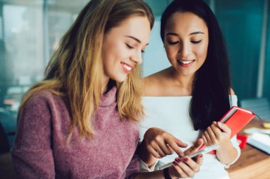 Çok ırklı içerik sahibi, günlük giysiler içinde, cep telefonu ekranına bakıp gülümseyen, beyin fırtınası yapan ve başarılı bir projede işbirliği yapan kadın iş arkadaşları.