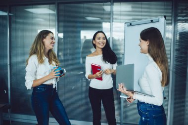 Modern ofiste dururken yeni projeyle ilgili iş arkadaşlarıyla konuşurken elinde dizüstü bilgisayarla gezen zeki genç iş kadını pozitifliği.