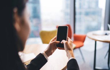 Çağdaş çalışma alanının bulanık arka planına karşı siyah ekranlı cep telefonuyla anonim kadın çalışan mesajlarının arka planı