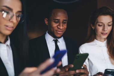 İş yerinde dikilip, karanlık odadaki ekrana bakarken cep telefonlarını karıştıran, resmi kıyafetler içinde konsantre olmuş çok ırklı iş arkadaşları.