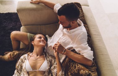 Mutlu erkek ve kadın sevgili, rahat koltukta dinlenirken flört ediyor, kaygısız çift ilişkiden bahsediyor ve gülümsüyor evde rahatlığın ve iletişimin tadını çıkarıyor.