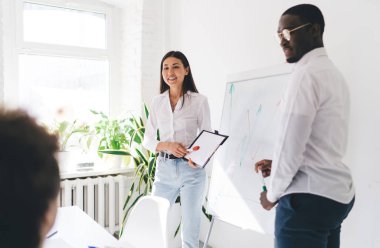 Gözlüklü ve şık giyinen Afro-Amerikan erkek çalışanlar, iş projesini ortaklarla tartışırken etnik iş arkadaşlarıyla birlikte duruyorlar.