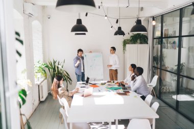 Çağdaş konferans salonunda cam duvarla toplanan çok ırklı takımın yüksek açılı görüntüsü.