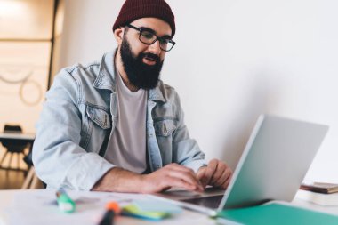 Günlük giysiler ve gözlüklü olumlu sakallı erkek yönetici ekrana bakarken ekranda otururken bulanık kalemli dokunmatik not defteri kullanıyor ve başlangıç ödevi üzerinde çalışıyor.