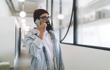 Ofiste çalışırken gülümseyen ve başka tarafa bakan sıradan giyinmiş, dalgın sakallı bir erkek çalışan.