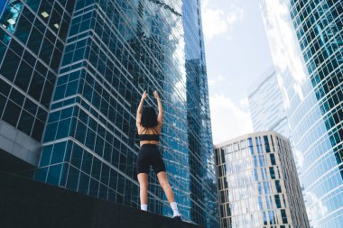 Modern şehrin merkezindeki gökdelenlere karşı çalışırken spor giyim sektöründe esneme egzersizleri yapan formda bir kadın modelin arka görüntüsü.