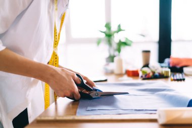 Tahta masanın yanında duran ve bulanık mağazalarda çalışırken makasla kumaş kesen tanınmayan kadın terzinin yan görüntüsü