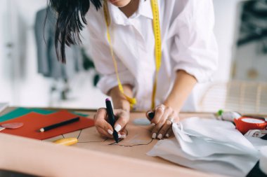 Beyaz gömlekli isimsiz kadın tasarımcı bant ölçme ve atölyede çalışırken kağıt üzerine çizim yapıyor.